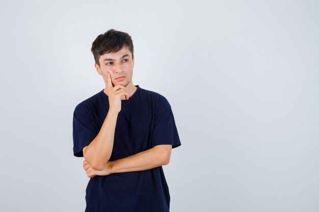 Homme brune debout dans la pensée pose en t-shirt sombre et à la vue sérieuse, de face.