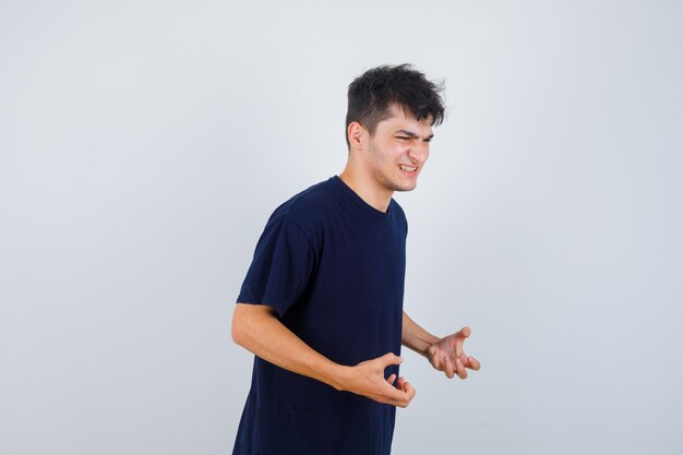 Homme brune gardant les mains de manière agressive en t-shirt et à l'ennui. vue de face.