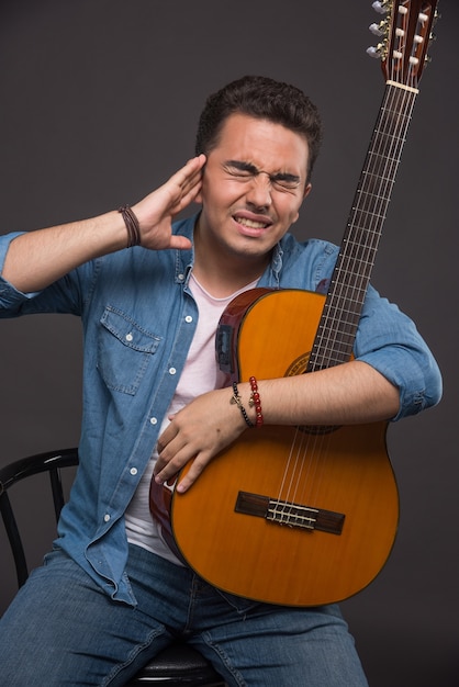 Homme brune avec guitare ayant des maux de tête fond sombre.