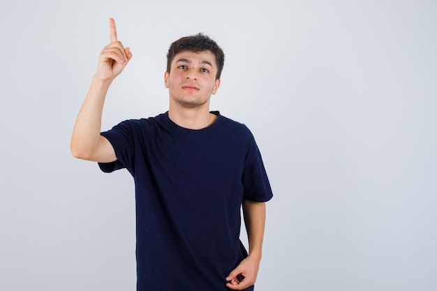 Homme brune pointant vers le haut en t-shirt et regardant prudente, vue de face.