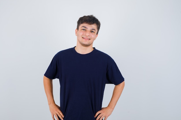 Homme brune posant avec les mains sur la taille en t-shirt et regardant joyeux, vue de face.