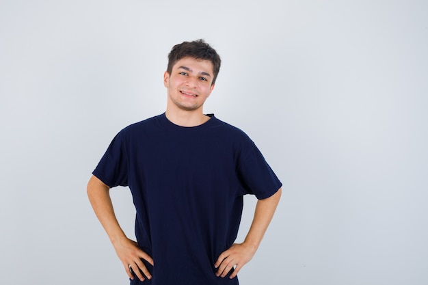 Homme brune posant avec les mains sur la taille en t-shirt et regardant joyeux, vue de face.