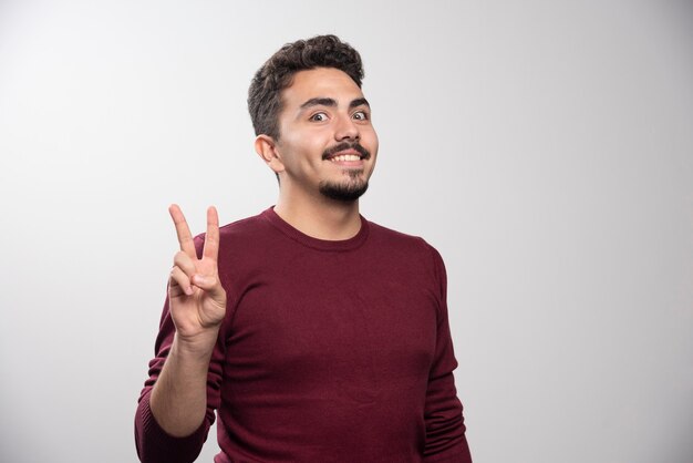 Un homme brune souriante montrant un signe de victoire.