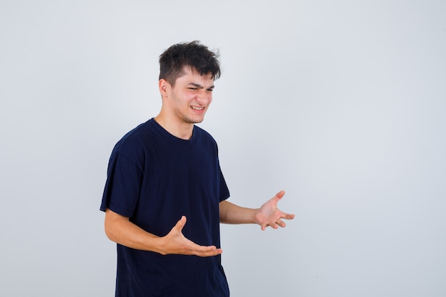 Homme brune en t-shirt faisant semblant de montrer quelque chose et regardant joyeux, vue de face.