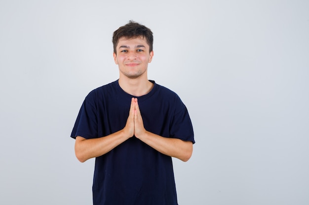 Homme brune en t-shirt sombre montrant le geste de namaste et à la vue détendue, de face.