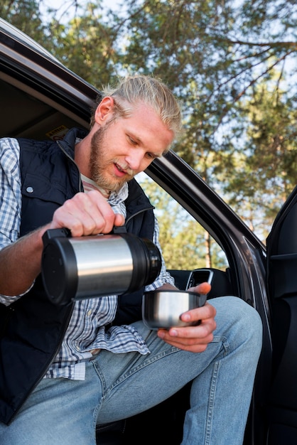 Photo gratuite homme buvant du café et assis à côté de la voiture