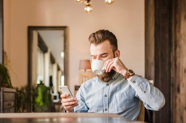 Homme buvant du café tout en utilisant un téléphone mobile