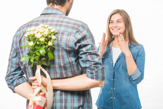 Homme cachant une fleur et cadeau derrière son dos devant une petite amie souriante