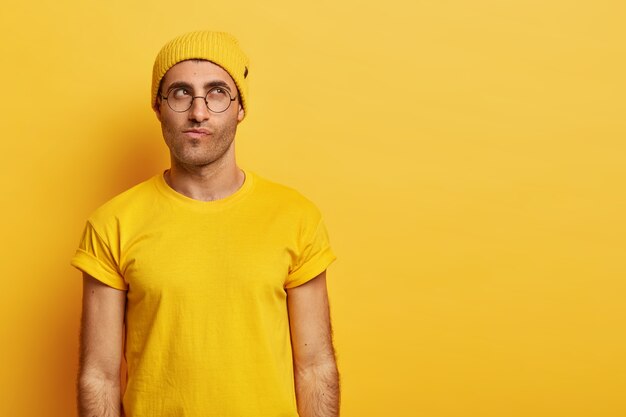 Un homme caucasien contemplatif regarde avec une expression réfléchie vers le haut, concentré au-dessus, serre les lèvres, essaie de prendre une décision