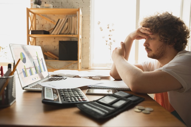 Photo gratuite homme caucasien contrarié et désespéré regardant des rapports financiers et économiques