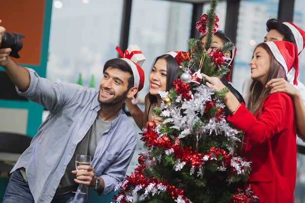 Un homme caucasien tenant une caméra prend un selfie avec des amis tout en célébrant la fête du nouvel an de noël