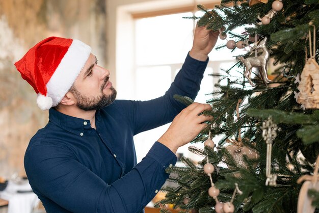 Homme avec chapeau de père Noël décorant un arbre