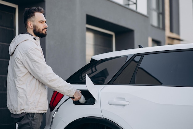 Homme chargeant une voiture électrique près de la maison