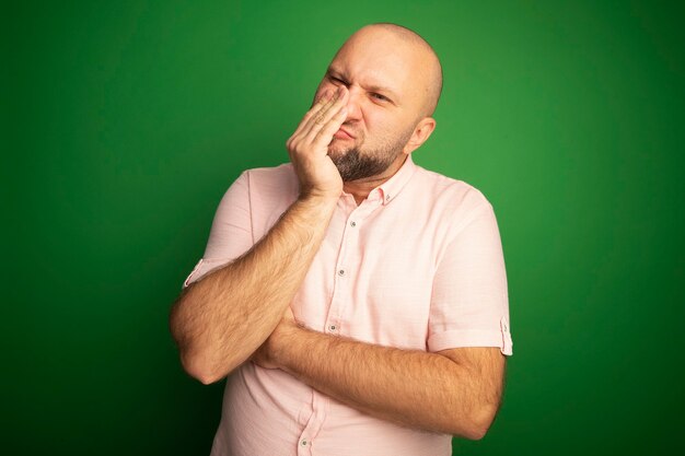 Homme chauve d'âge moyen insatisfait portant un t-shirt rose bouche couverte avec la main