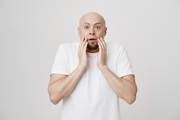 Homme chauve étonné haletant, toucher le menton et regarder