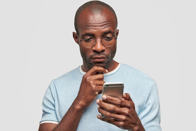 Homme chauve tient un téléphone intelligent, regarde attentivement l'écran du cellulaire, des textes avec un ami, lit le contenu du message