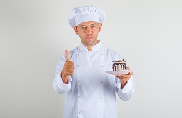 Homme chef cuisinier en chapeau et uniforme tenant le gâteau et montrant les pouces vers le haut