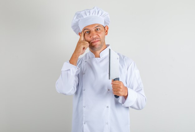 Homme chef cuisinier tenant un couteau pour la viande et penser en uniforme et chapeau et à la recherche positive