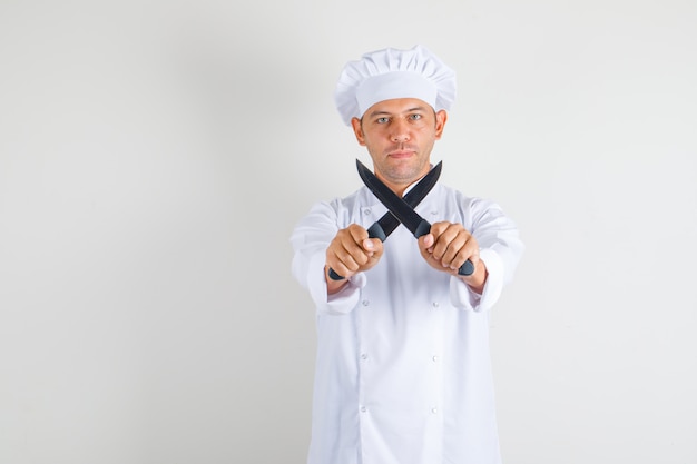 Homme chef cuisinier tenant des couteaux et regardant la caméra en chapeau et uniforme