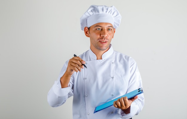 Homme chef tenant stylo et presse-papiers en uniforme et chapeau et à la surprise