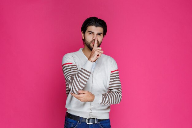 L'homme en chemise blanche fait signe de se taire et d'arrêter de parler.