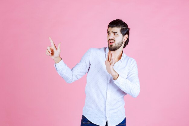 Homme en chemise blanche levant la main pour attirer l'attention ou montrer quelque chose.