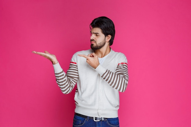 Homme en chemise blanche pointant et présentant quelque chose sur le côté gauche.