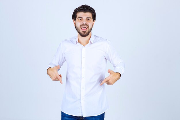 Homme en chemise blanche pointant quelque part en dessous.