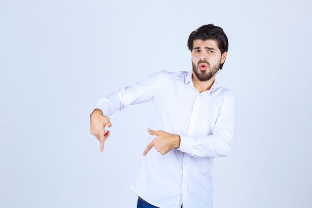 Homme en chemise blanche pointant quelque part en dessous.