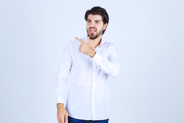 Homme en chemise blanche pointant quelque part sur la gauche avec des émotions de visage.