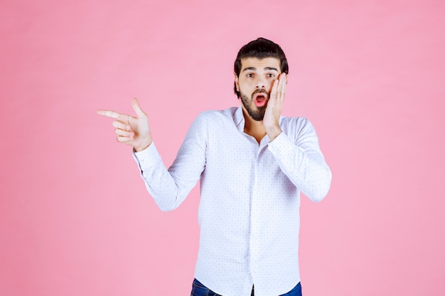 Homme en chemise blanche pointant vers le côté gauche.