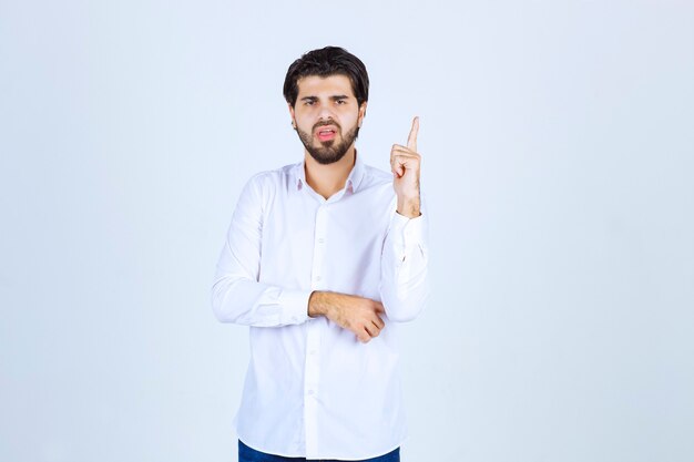 Homme en chemise blanche pointant vers le haut.