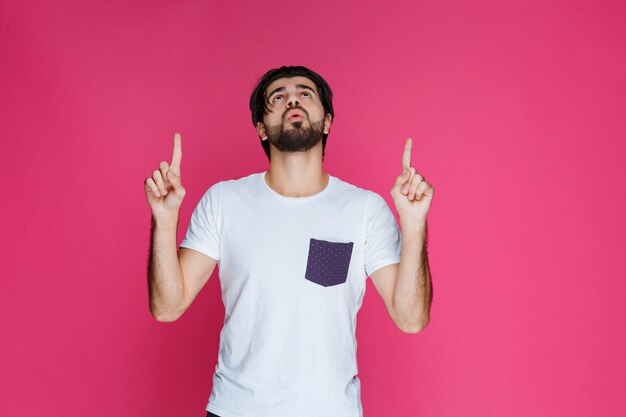 Homme en chemise blanche pointant vers quelque chose au-dessus.