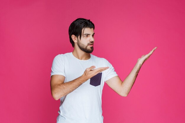 Homme en chemise blanche pointant vers quelque part et présentant quelqu'un ou montrant simplement la direction.