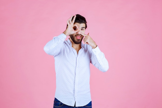 Homme en chemise blanche regardant à travers ses doigts.