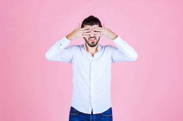 Homme en chemise blanche regardant à travers ses doigts.