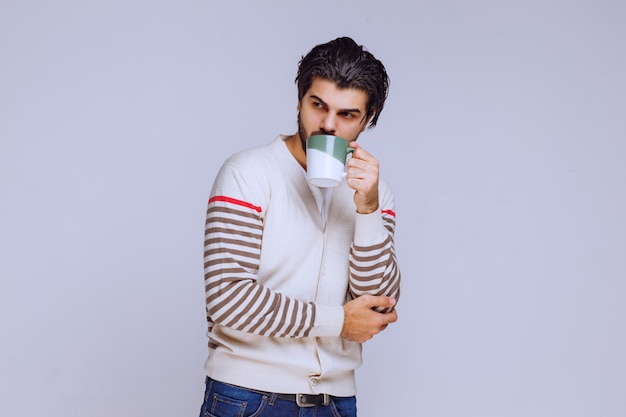 Homme en chemise blanche tenant et posant avec une tasse de café.