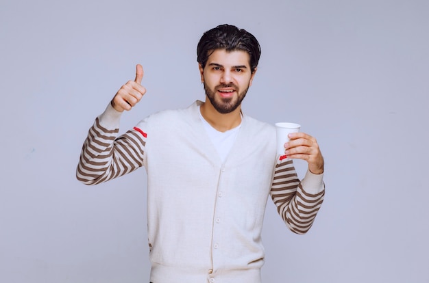Homme en chemise blanche tenant une tasse de café et faisant un bon signe de la main.