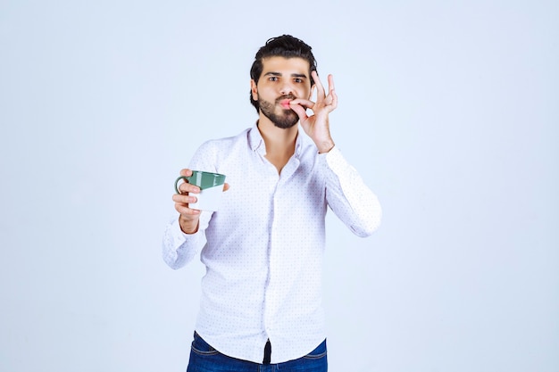 Homme en chemise blanche tenant une tasse de café et en profitant.