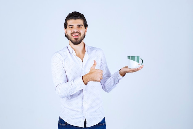 Homme en chemise blanche tenant une tasse de café et en profitant.