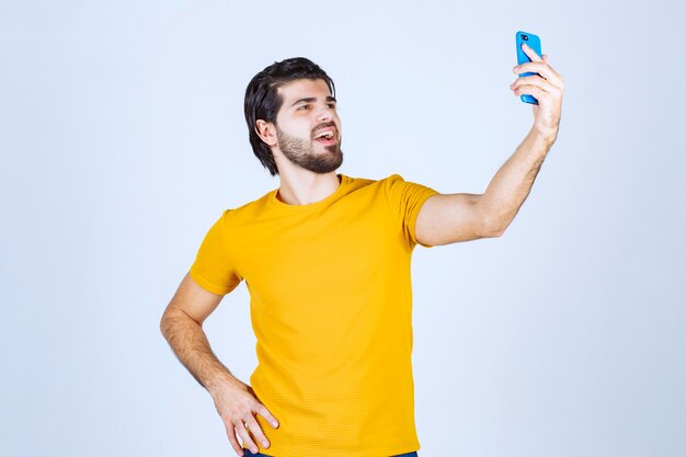 Homme en chemise jaune tenant un smartphone bleu.