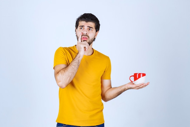 Homme en chemise jaune tenant une tasse rouge et pensant.