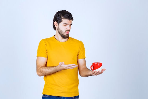 Homme en chemise jaune tenant une tasse rouge et pensant.