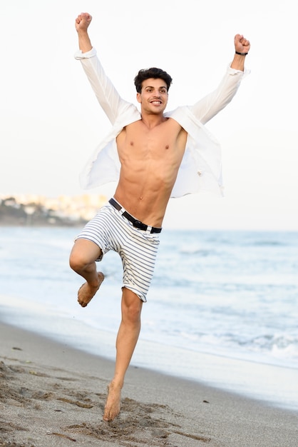 L&#39;homme avec la chemise ouverte sur la plage et une jambe levée