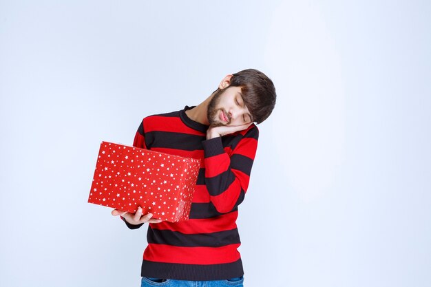 L'homme En Chemise Rayée Rouge Avec Une Boîte-cadeau Rouge A L'air Somnolent Et épuisé.