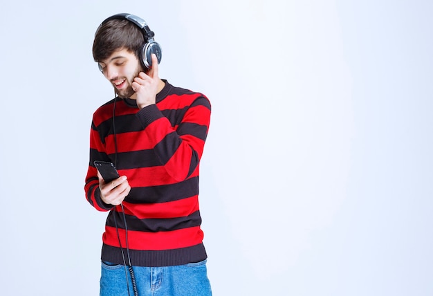 Photo gratuite homme en chemise rayée rouge écoutant des écouteurs et définissant la musique de sa liste de lecture sur le smartphone.