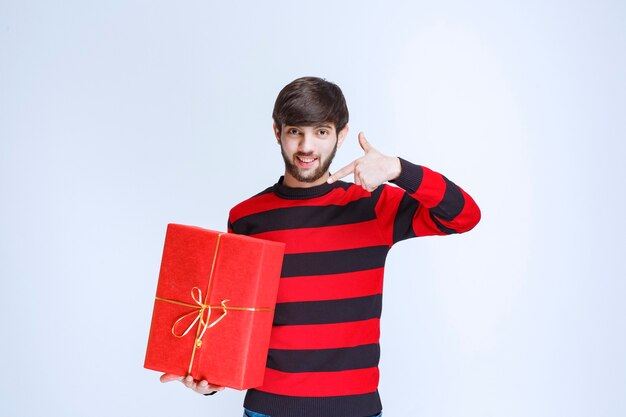 Homme en chemise rayée rouge tenant une boîte-cadeau rouge et en faisant la promotion.