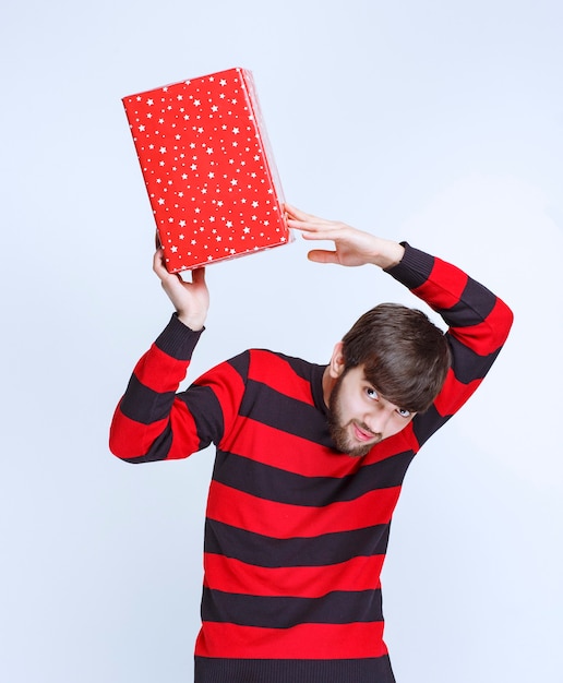 Homme en chemise rayée rouge tenant une boîte-cadeau rouge, la livrant et la présentant