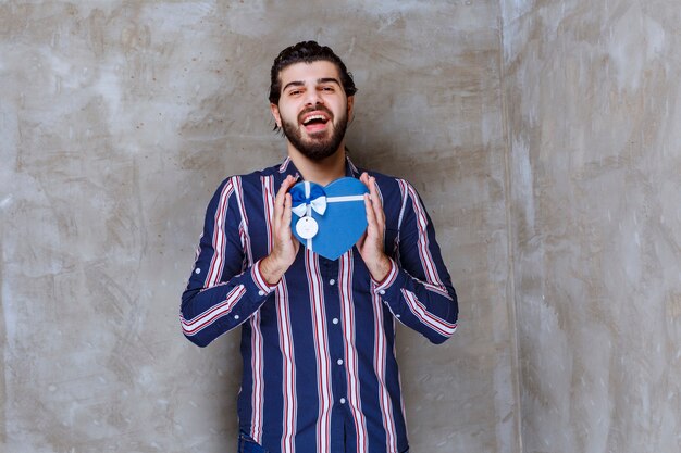Homme en chemise rayée tenant une boîte cadeau en forme de coeur bleu
