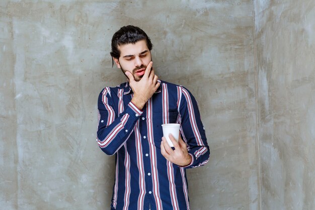 Homme en chemise rayée tenant une tasse d'eau jetable blanche et réfléchissant à la façon de la vendre